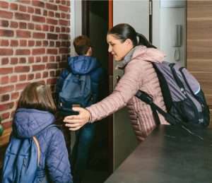 A mother with dark hair rushing two children into school