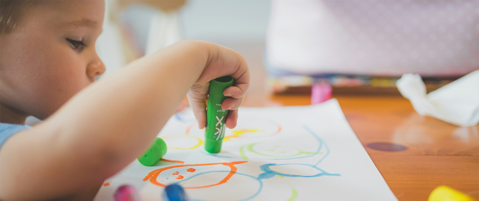 A small light haired child using a green marker on white paper