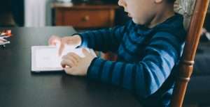 Small boy sitting at a dining room table using a tablet computer 