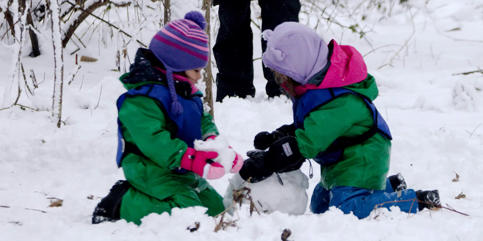 Two small children in snowsuits making a snowman