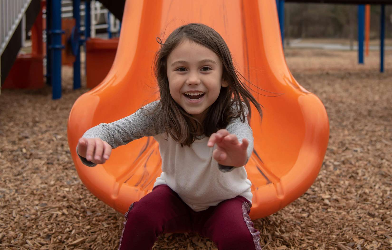 Smiling young girl with dark hair at the bottom of an orange slide.